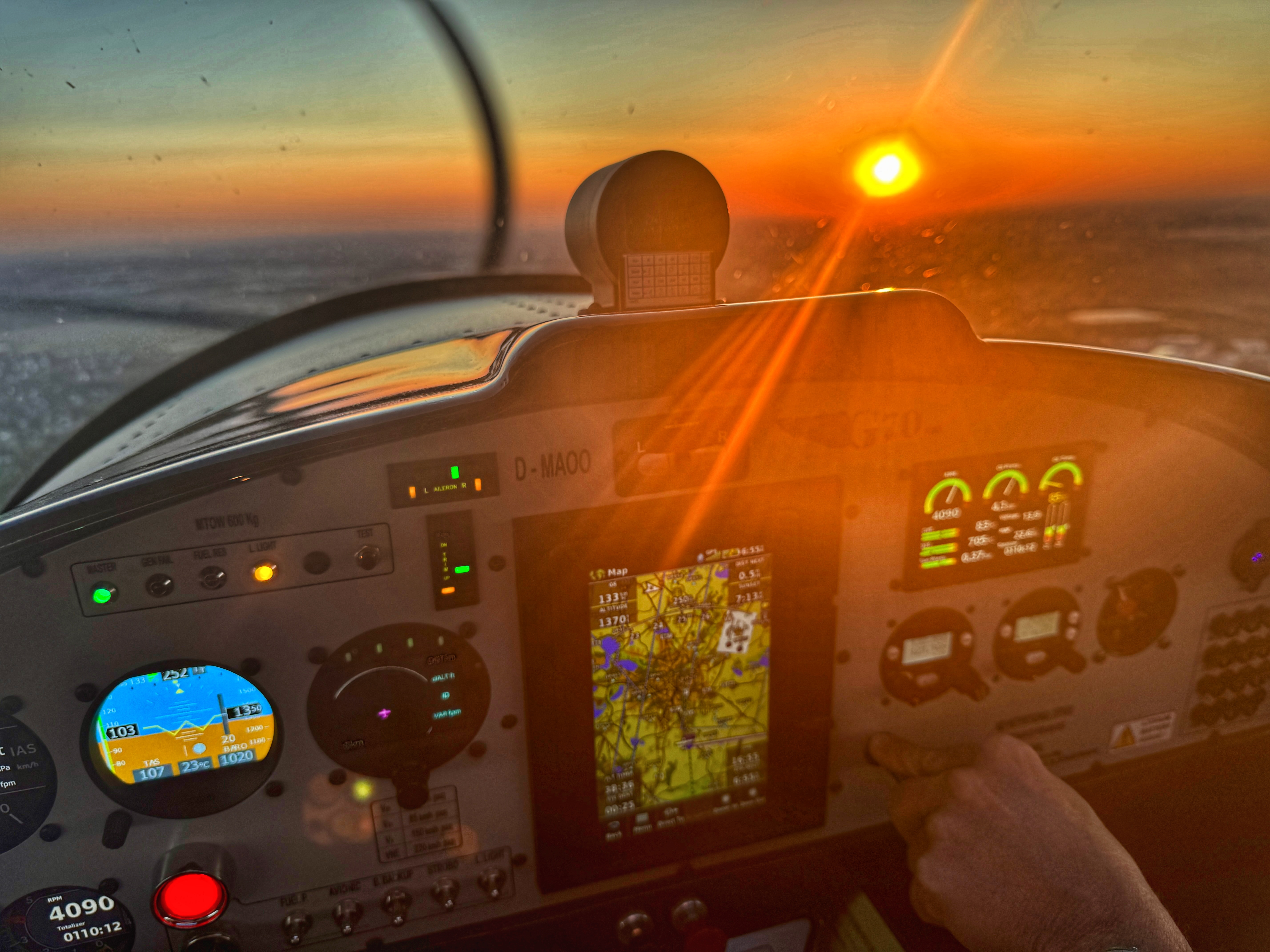 Blick auf das Cockpit eines Flugzeugs bei Sonnenuntergang, mit beleuchtetem Instrumentenpanel und GPS-Anzeige.
