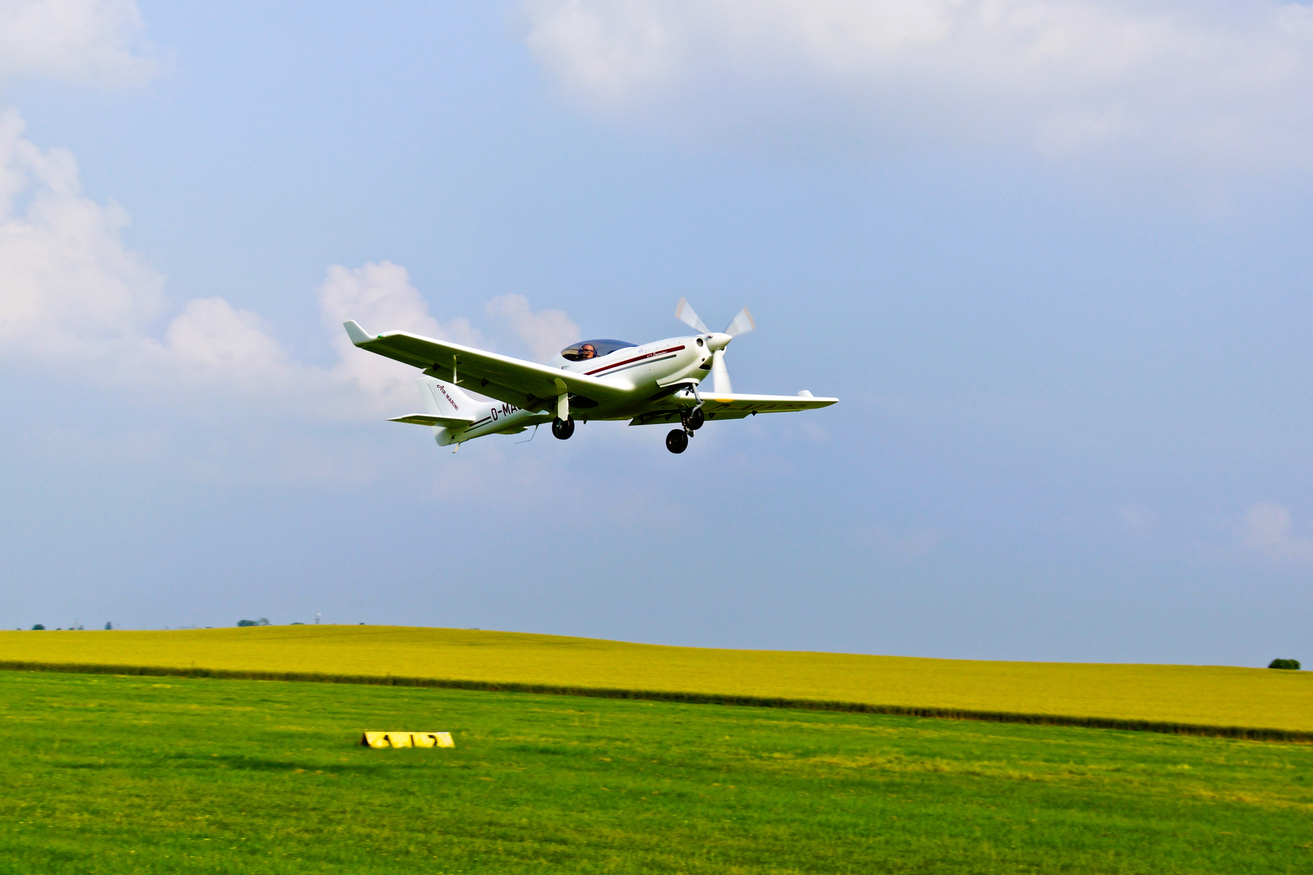 Kleinflugzeug kurz vor der Landung auf einem grünen Feld unter blauem Himmel