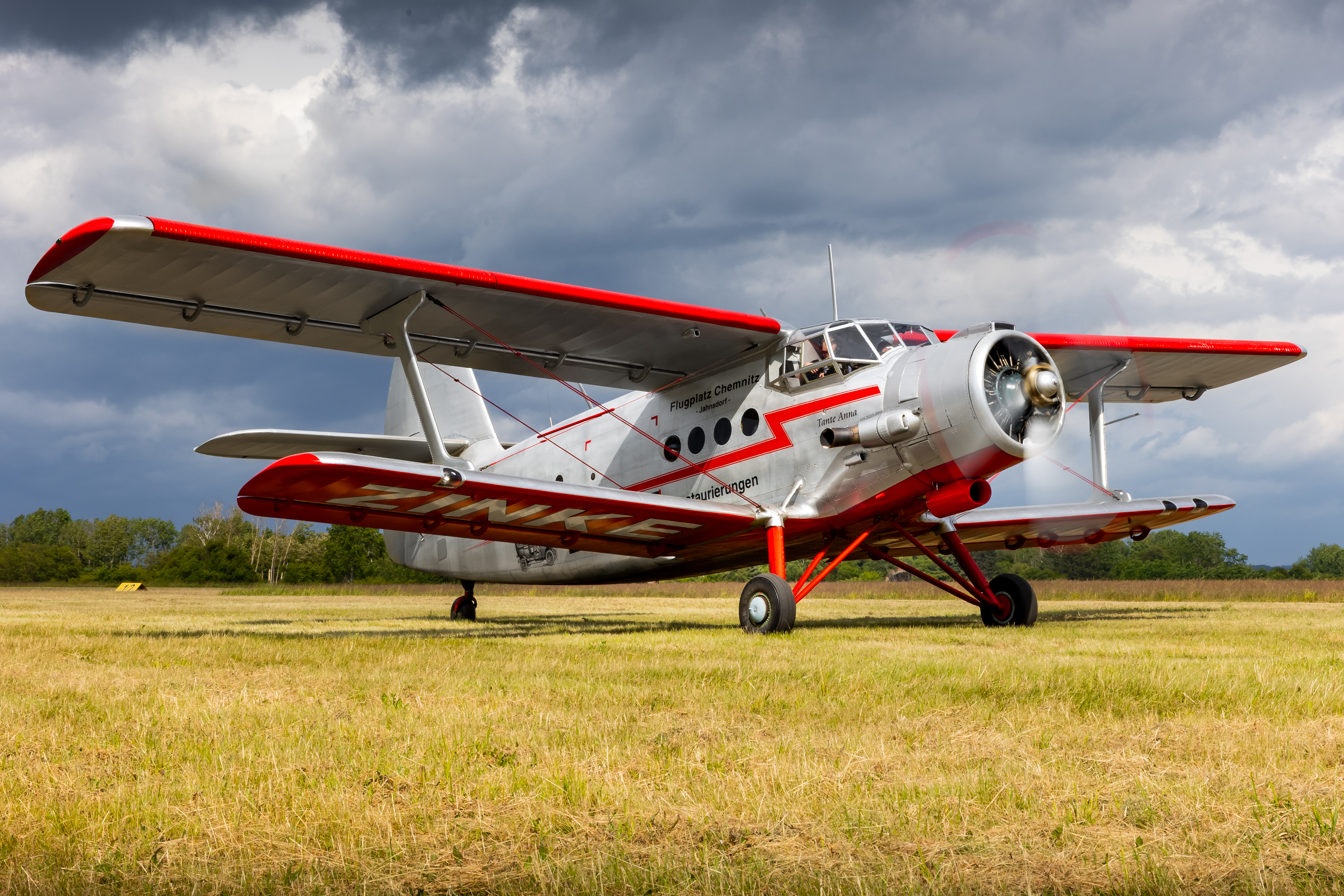 Ein historisches Doppeldecker-Flugzeug mit rot-weißer Lackierung steht auf einem Flugplatz unter bewölktem Himmel.