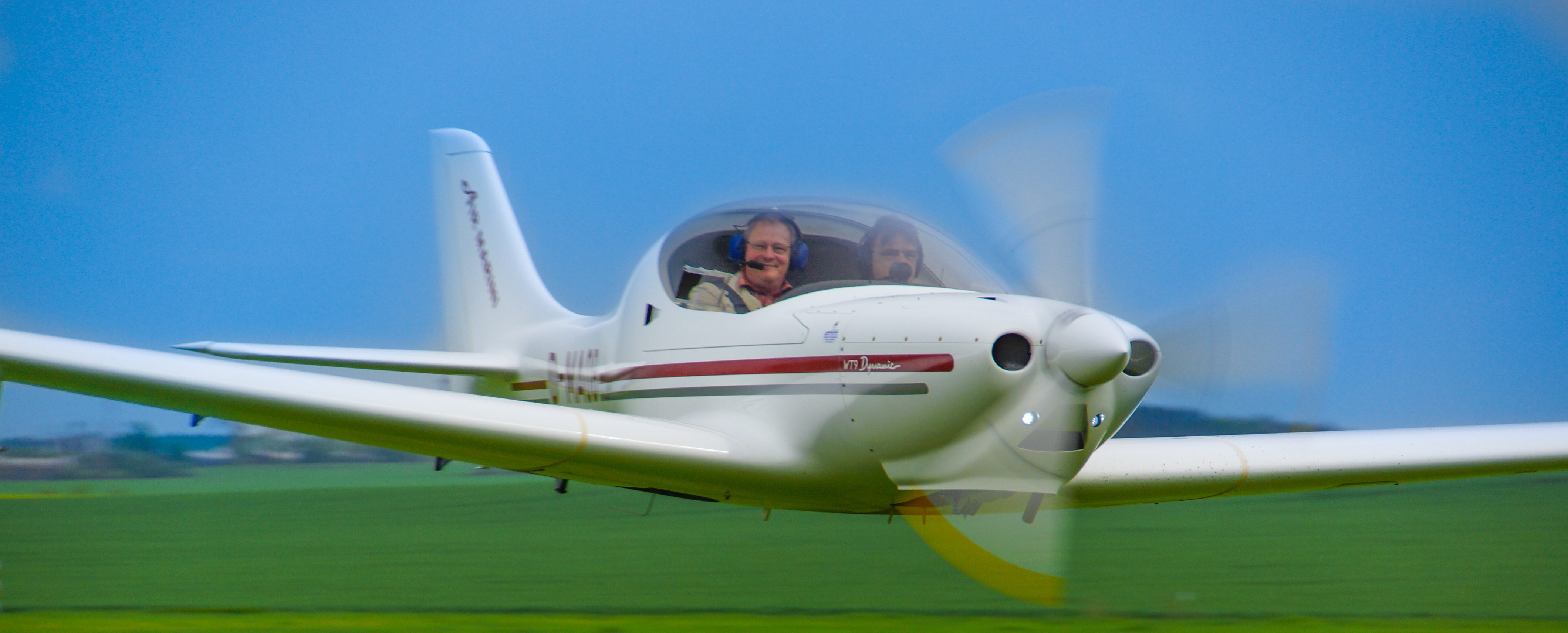 Zweisitziges Sportflugzeug fliegt tief über grüne Wiese