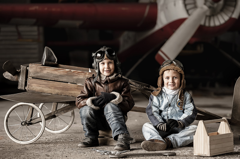 Zwei Kinder mit Fliegerhauben vor einem Flugzeug und einem Spielzeugflieger