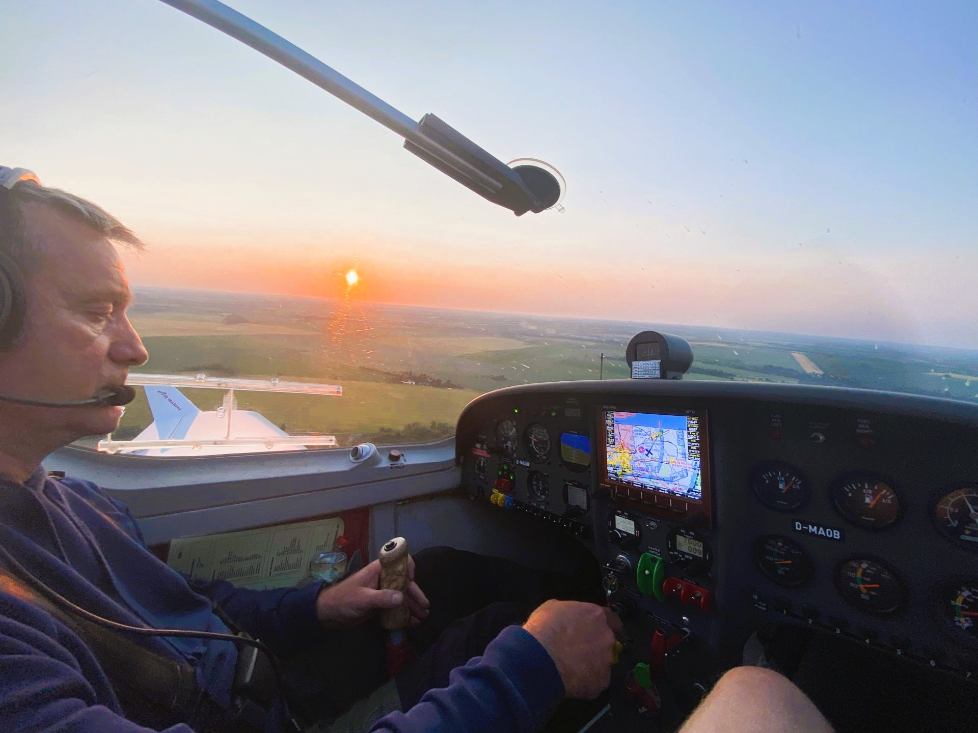 Pilot steuert ein kleines Flugzeug bei Sonnenuntergang, mit Blick auf Instrumentenbrett und Landschaft