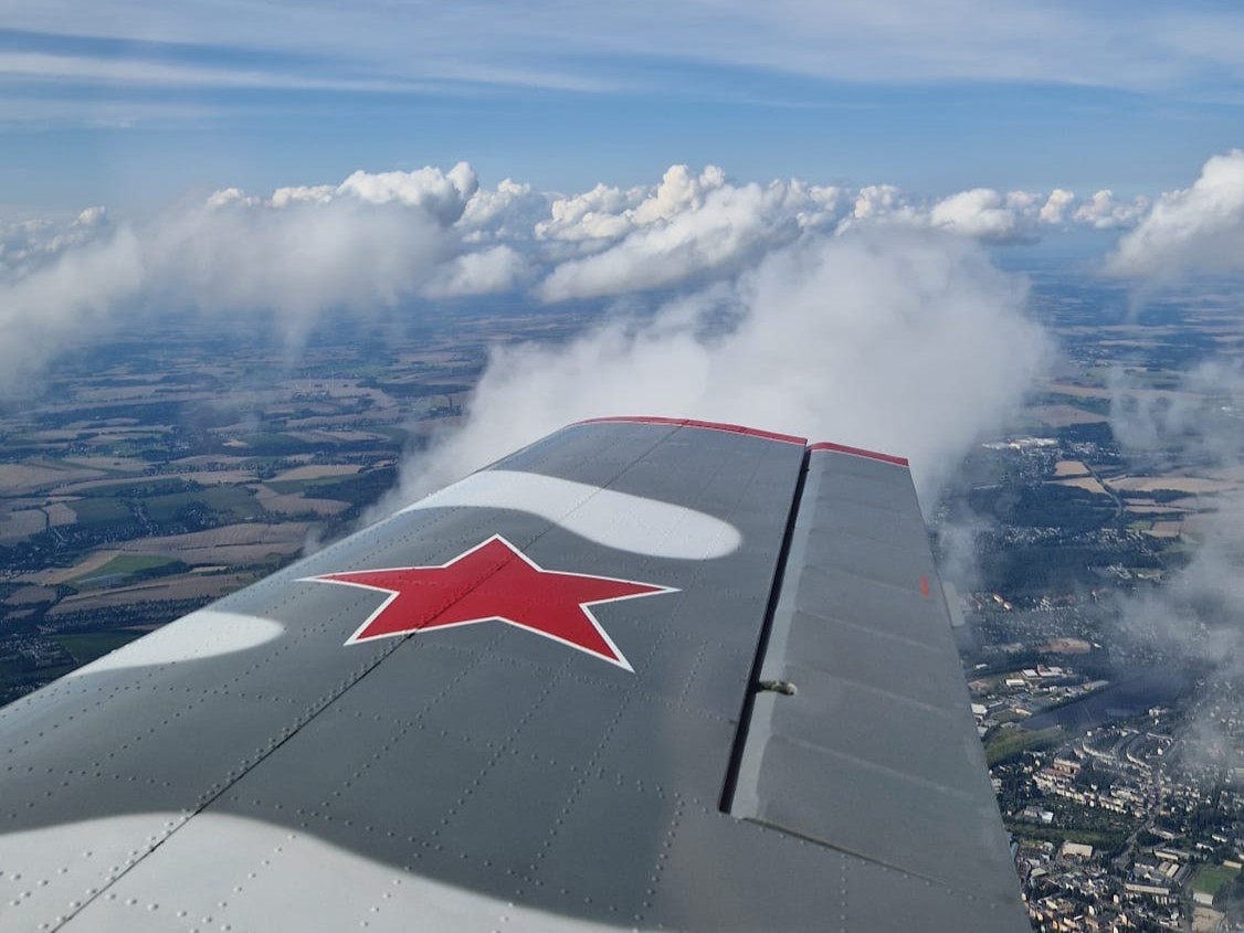 Flugzeugflügel mit rotem Stern über Wolken und Landschaft
