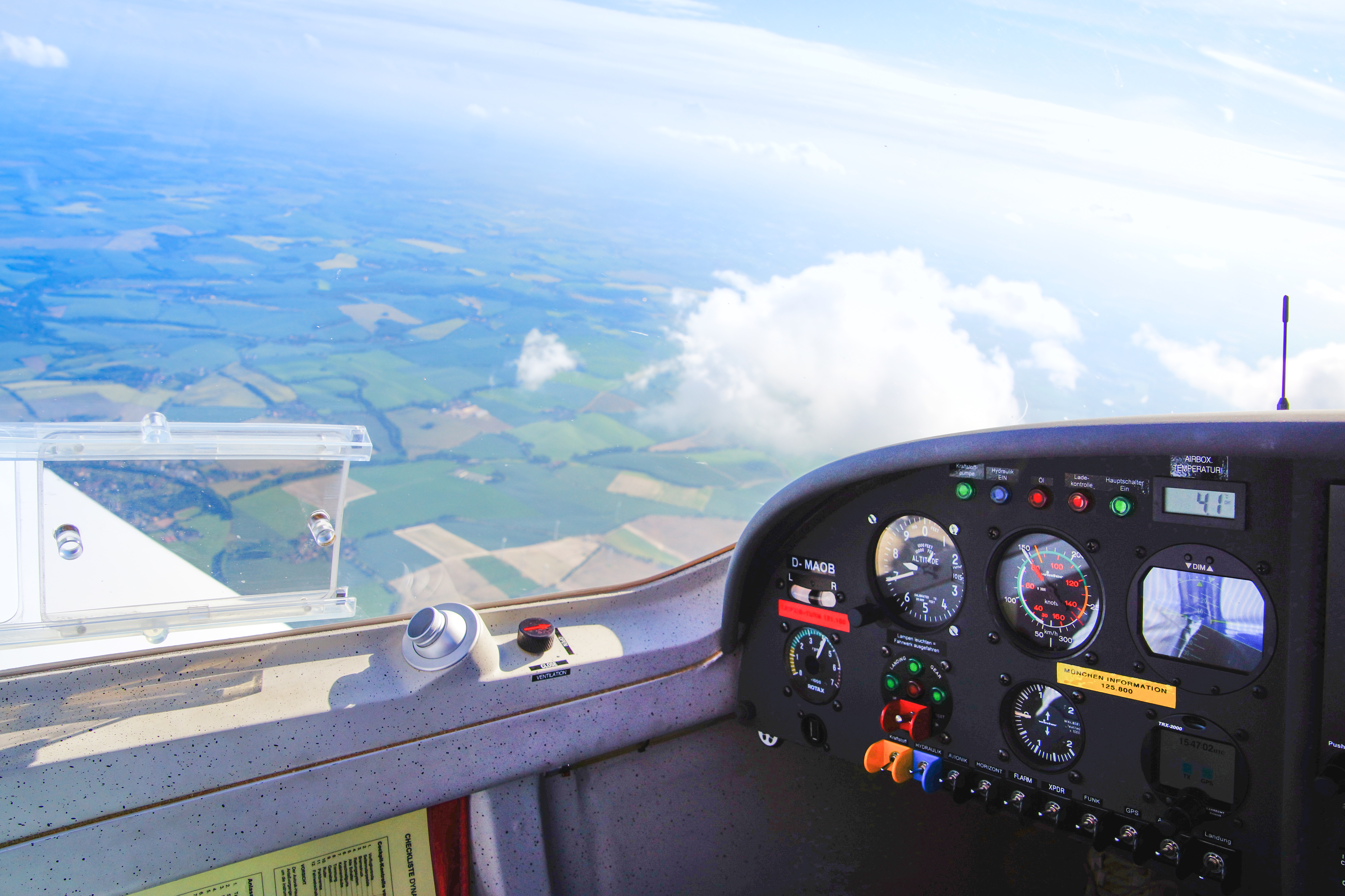 Ansicht des Cockpits eines Leichtflugzeugs mit Instrumententafel, fliegender über eine grüne Landschaft unter blauen Himmel und Wolken
