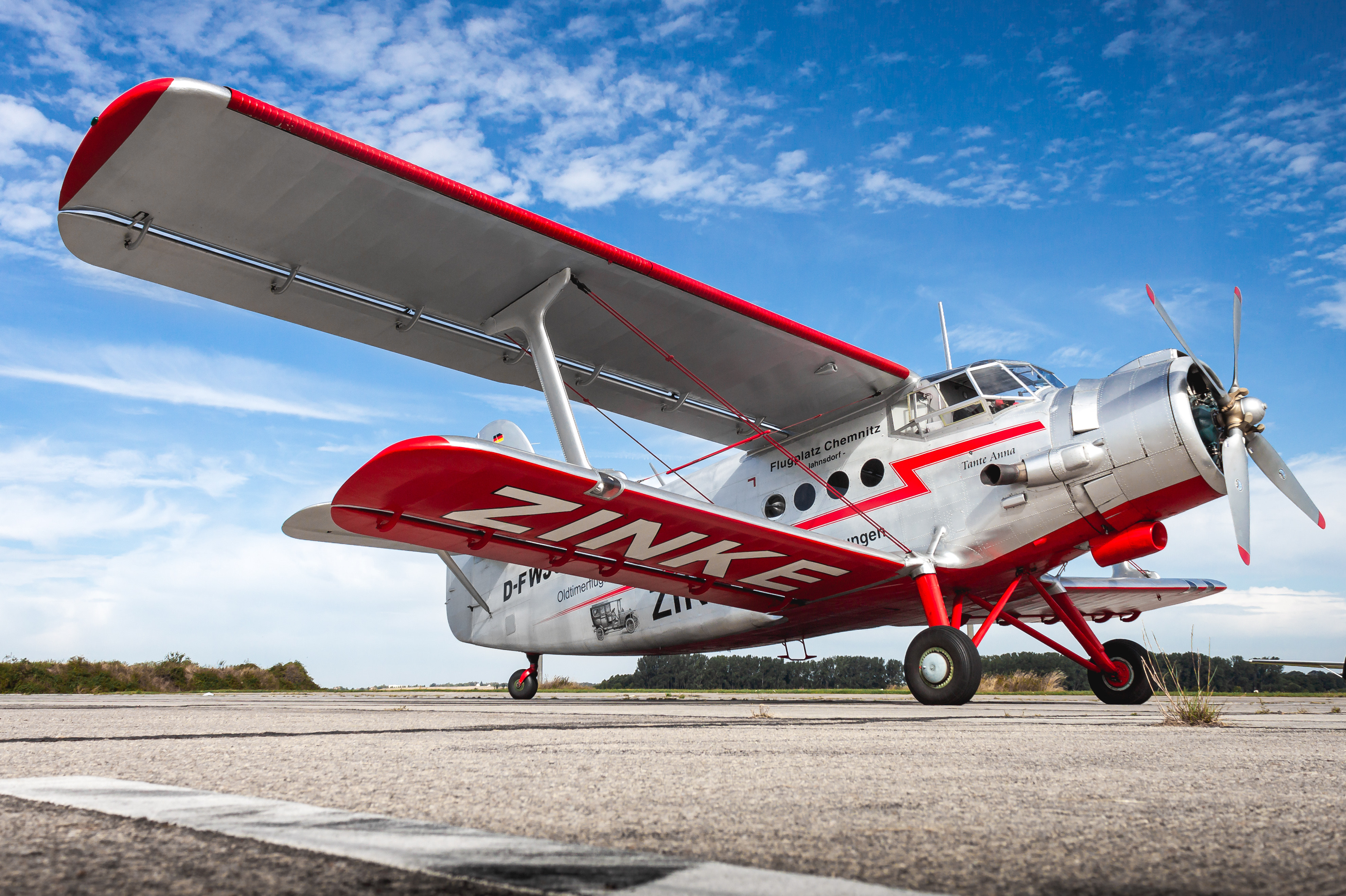 Ein rot-weißes Doppeldeckerflugzeug steht auf einer Landebahn unter blauem Himmel.