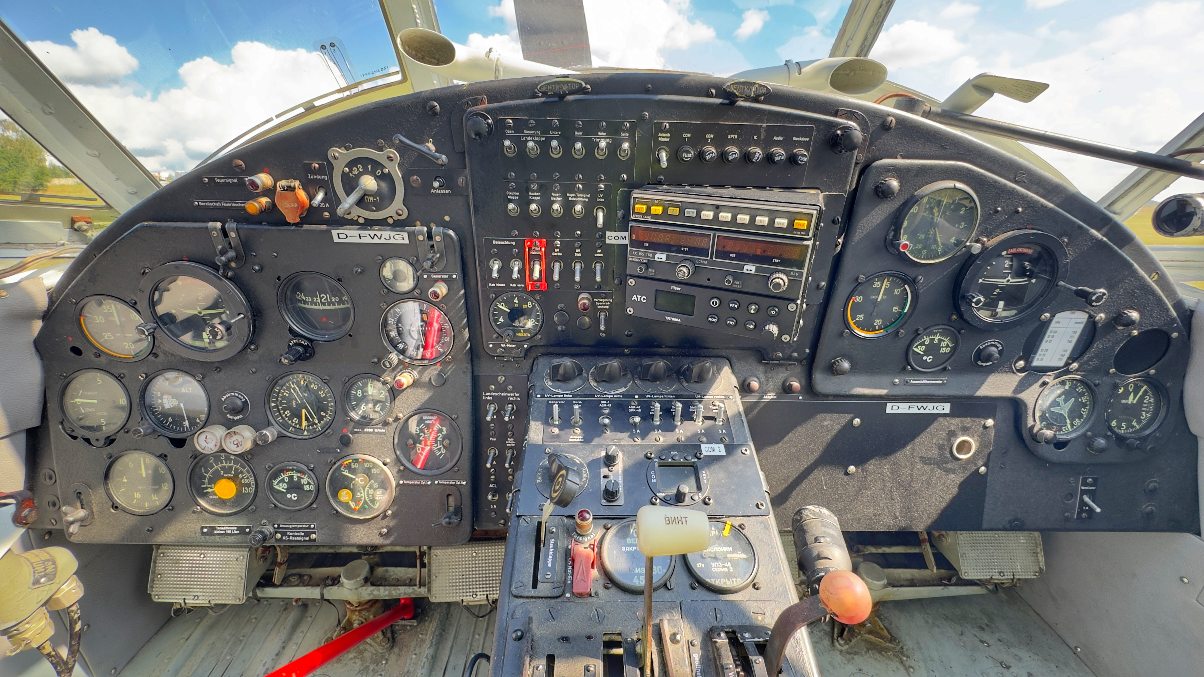 Cockpit eines Oldtimer-Flugzeugs mit analogen Instrumenten und zahlreichen Schaltern, die eine historische Atmosphäre widerspiegeln. Außenansicht durch die Glasfenster.