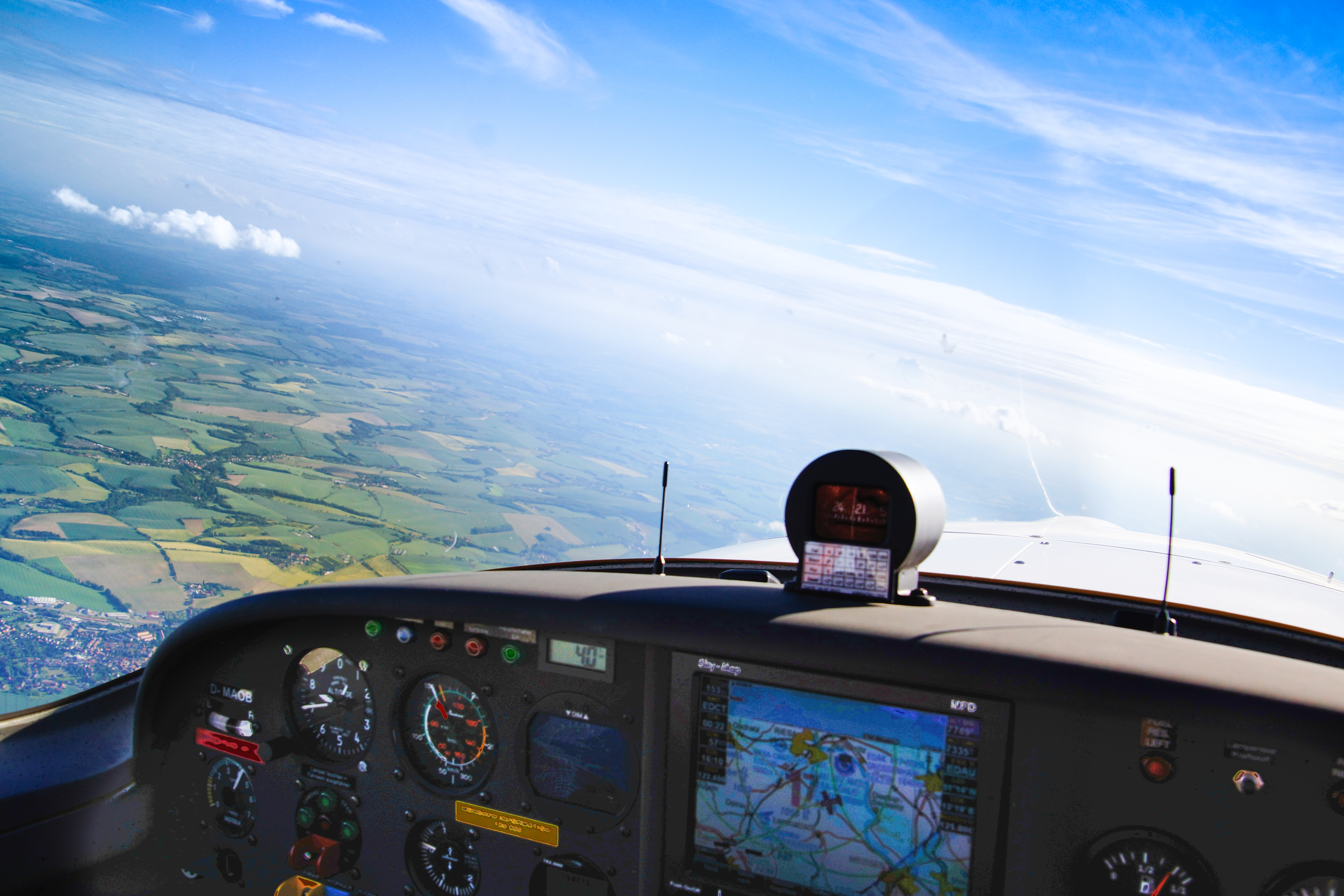 Blick aus dem Cockpit eines Flugzeugs auf eine weitläufige grüne Landschaft bei klarem Himmel und Sonnenschein