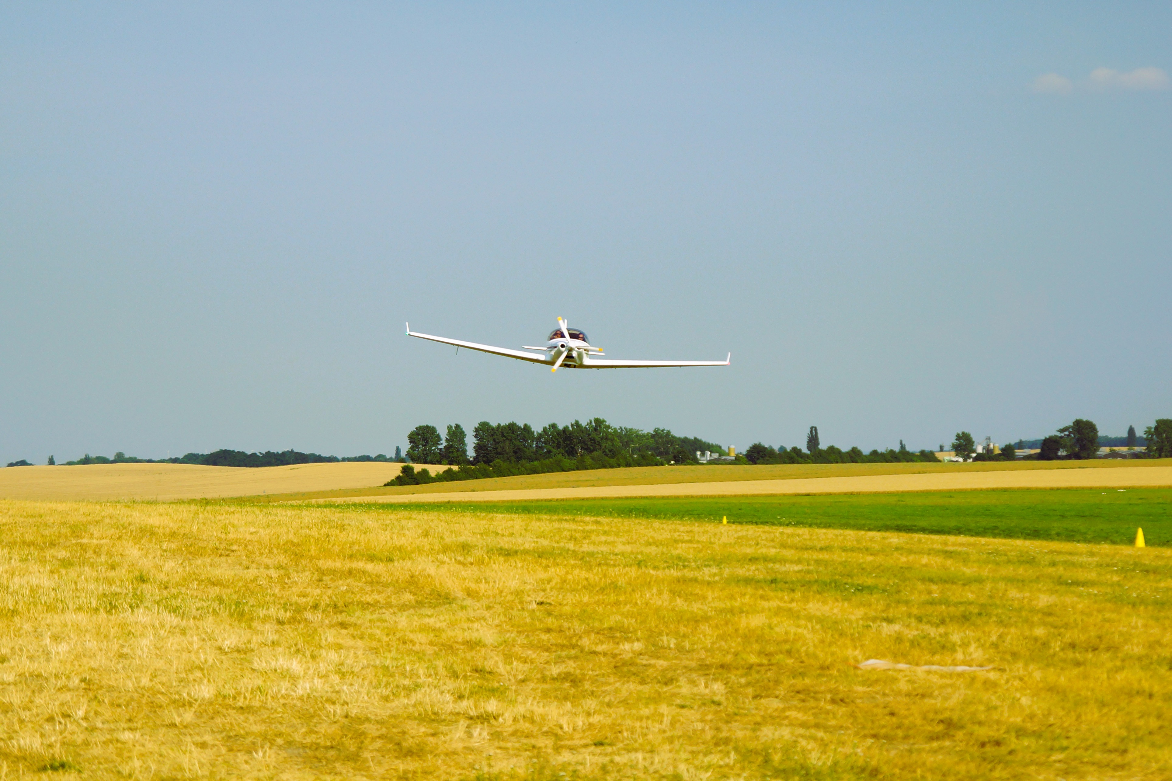 Ein kleines Flugzeug fliegt über ein ländliches Feld, umgeben von Bäumen im Hintergrund